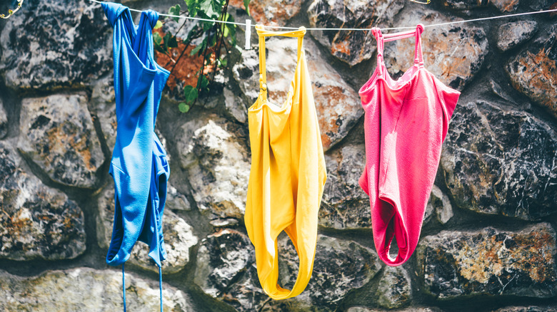 Wet swimsuits hanging on a clothesline against a stone wall.