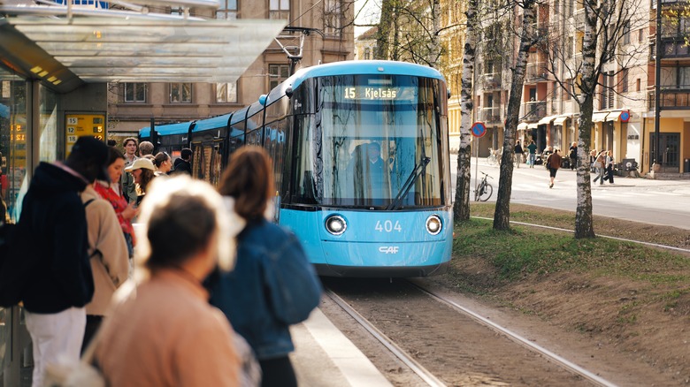 A blue tram pulling up to a crowded station in Oslo