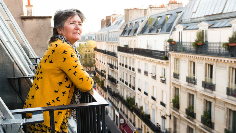 Older woman standing on a balcony over a street in Paris
