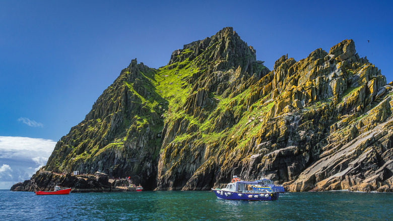 Cruise boats filled with tourists dock at Skellig Michael island, a UNESCO World Heritage site off of County Kerry, Ireland, on a bright summer day