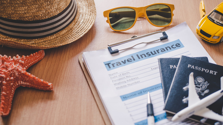 Desk with travel insurance documents on it, along with passports, pen, sunglasses, hat, toy car, and starfish