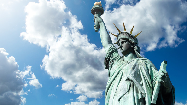 Close-up of the Statue of Liberty in New York, photographed against a bright blue, cloud-filled sky