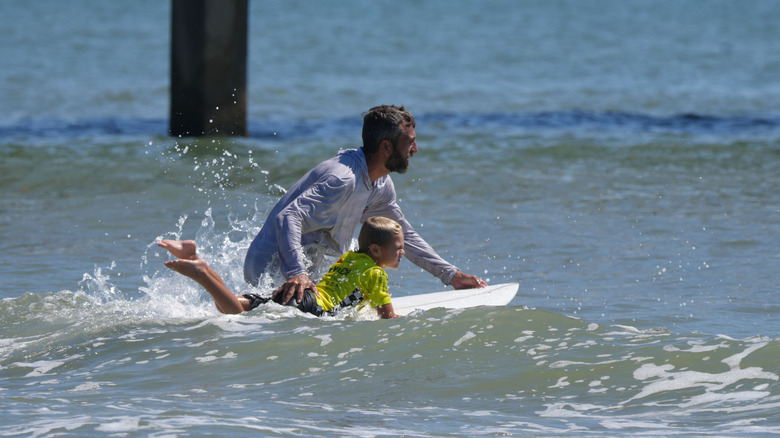 Father pushes young son on a wakeboard into the surf