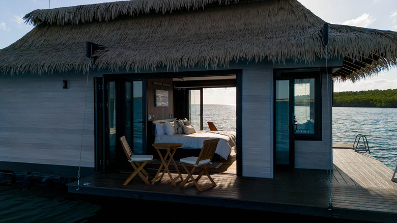 looking through the windows of an overwater bungalow with a king-size bed and a view of the sea and mangroves on the other side