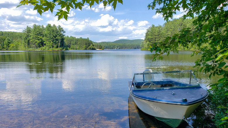 A calm lake surrounded by green trees with a small blue boat tied close to shore in Barry's Bay, Ontario