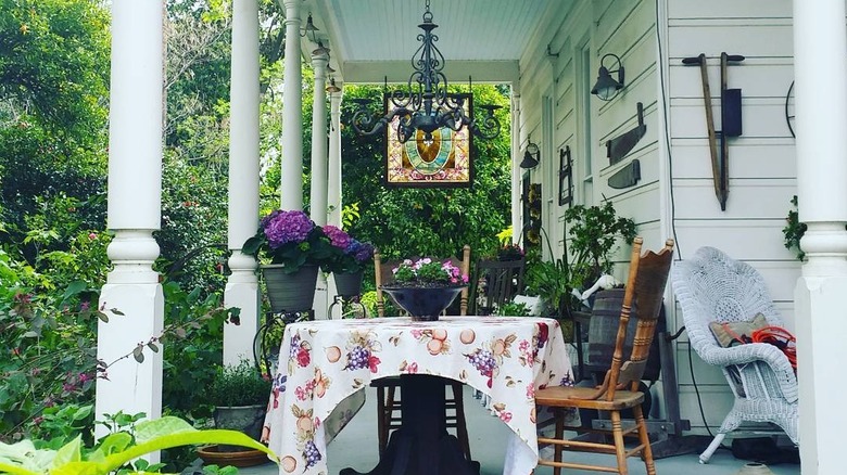 white house with wood chairs at table with flowers on it green trees