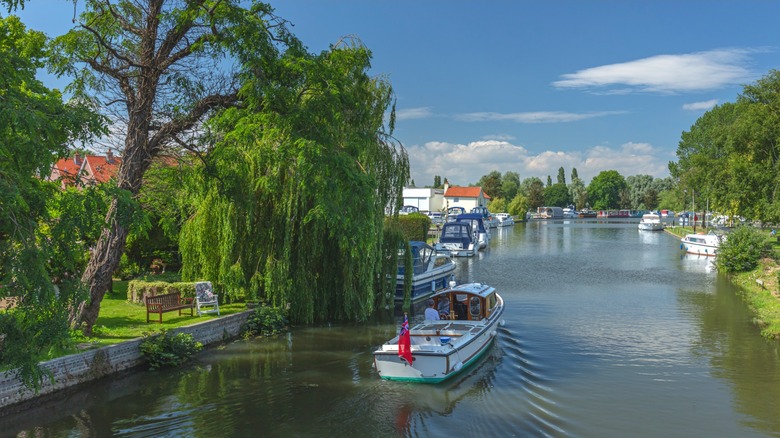 A motorboat cruising the River Waveney flanked by boats and emerald trees in Beccles, England