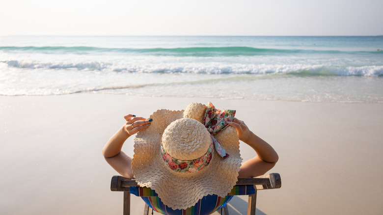 A woman sitting on a beach chair holding her floppy hat