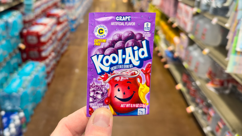 Someone holding up a packet of grape Kool-Aid in a grocery store