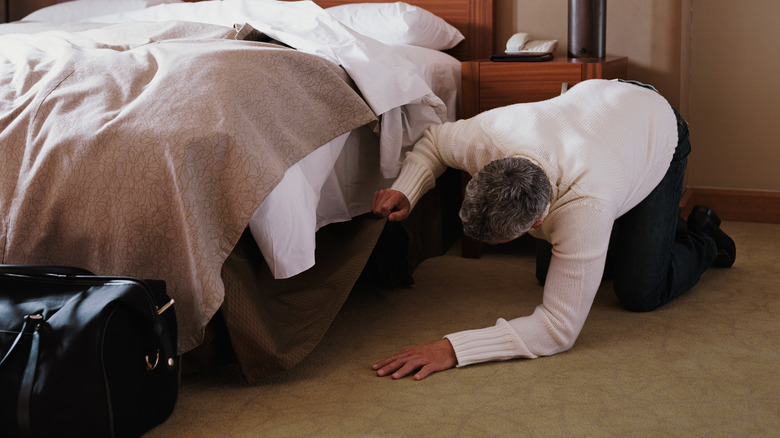 touching hotel carpet and peering under bed