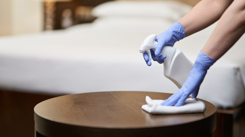 gloved hands spraying hotel room sanitizer 