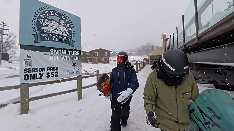 Snowboarders walking past a $52 season pass sign for snow tubing at Greek Peak