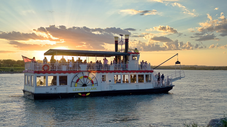 Bismarck's Lewis & Clarke Riverboat cruising down the Missouri River while the sun sets behind clouds.