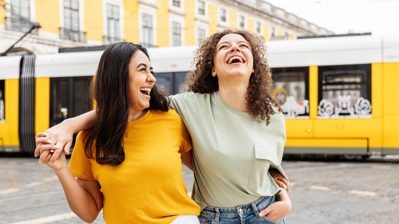 Two smiling friends standing in front of Lisbon's yellow tram and buildings