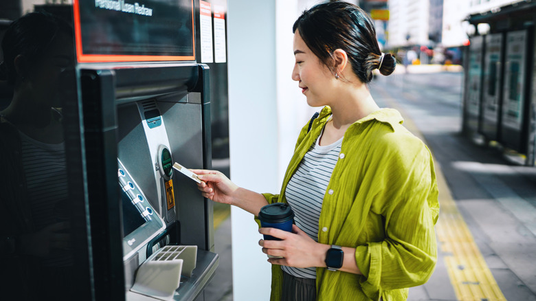 Young woman in yellow shirt inserting bank card into ATM machine