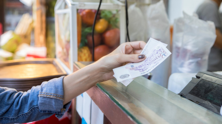 A woman's hand extending foreign currency to a cashier at a market