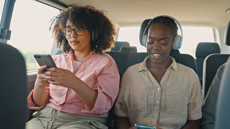 Two women on phones while sitting in the back of moving car.