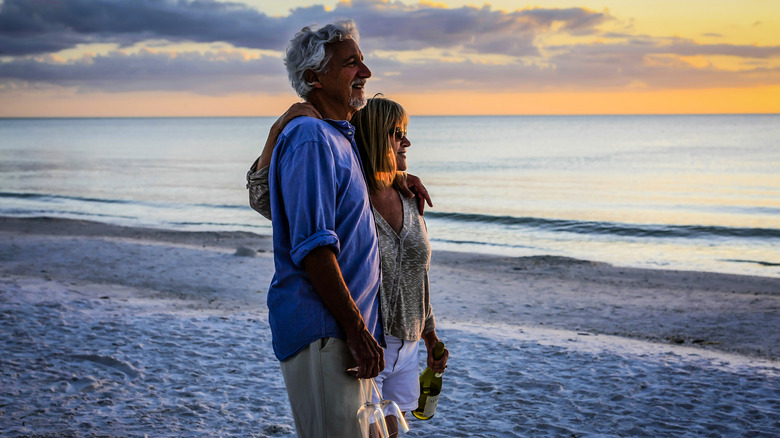 A mature couple on the beach with a bottle of wine and glasses in hand