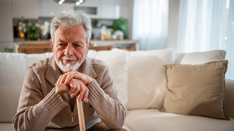 A senior man on a couch in a home holding a walking stick