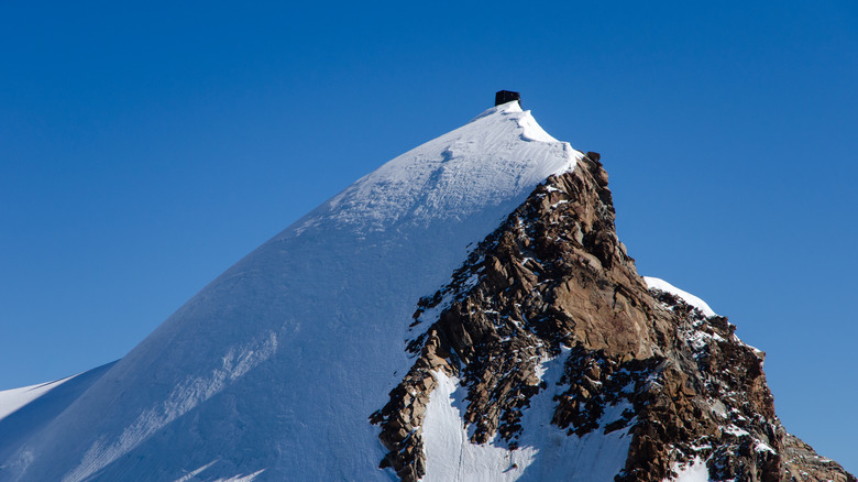 Tiny mountain hut perched on top of a snowy mountain peak