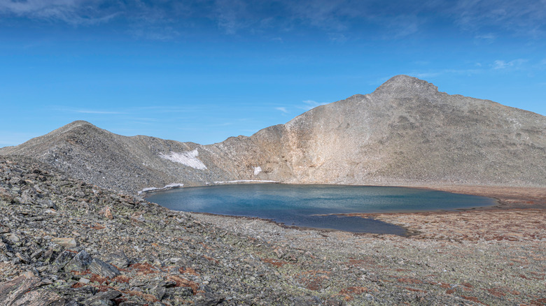 Pacific Tarn lake lies between rocky peaks under a bright blue sky in Colorado