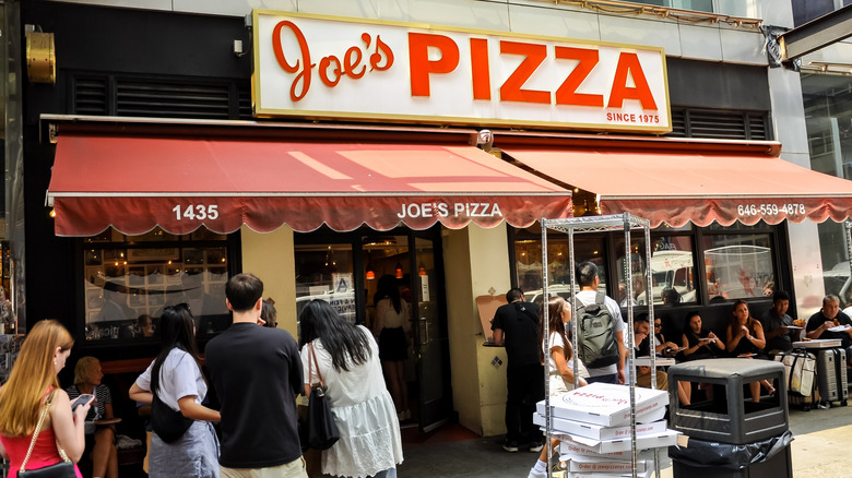 Joe's Pizza storefront, customers standing and sitting outside