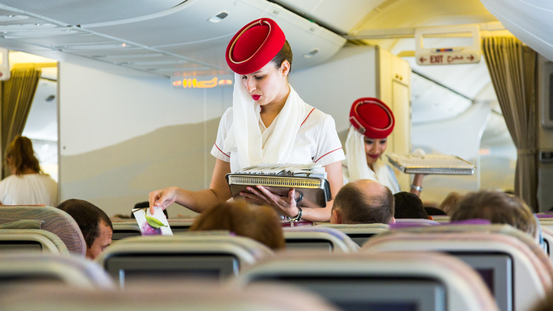 Two Emirates cabin crew handing out menus to passengers in their seats