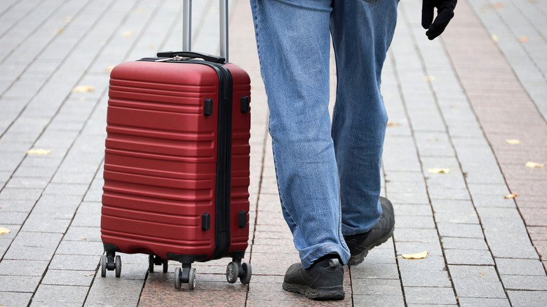 Legs of man wheeling a red rolling suitcase