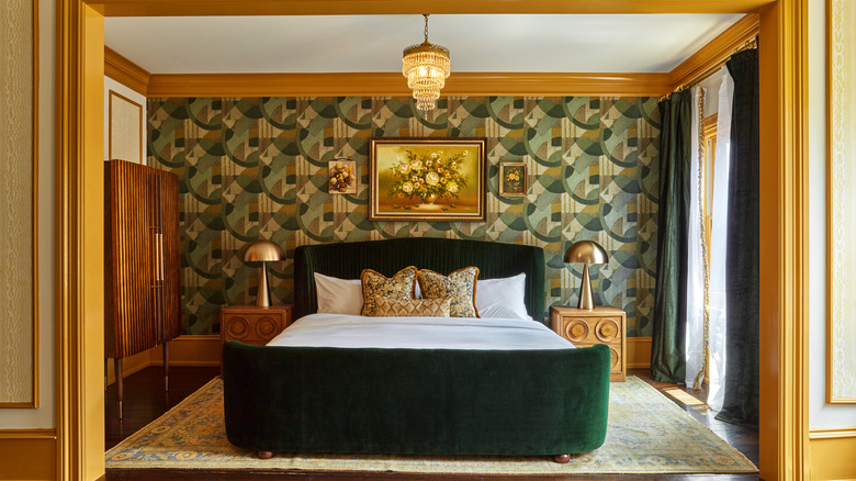 Hotel bed with velvet green headrest, art deco wall paper, crystal chandelier, and gold trim