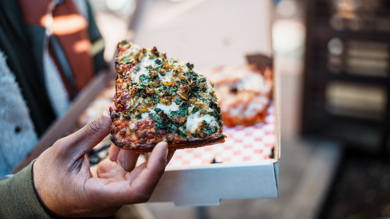 A person holds a folded slice of pizza and a pizza box.