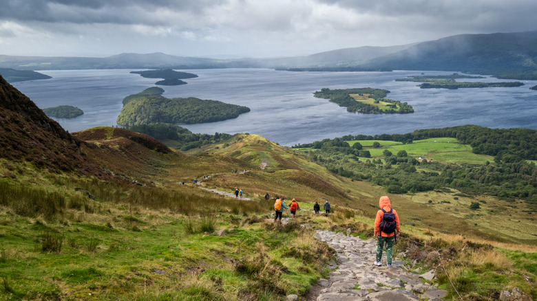 Hikers descent a path that has sweeping views over island-dotted Loch Lomond