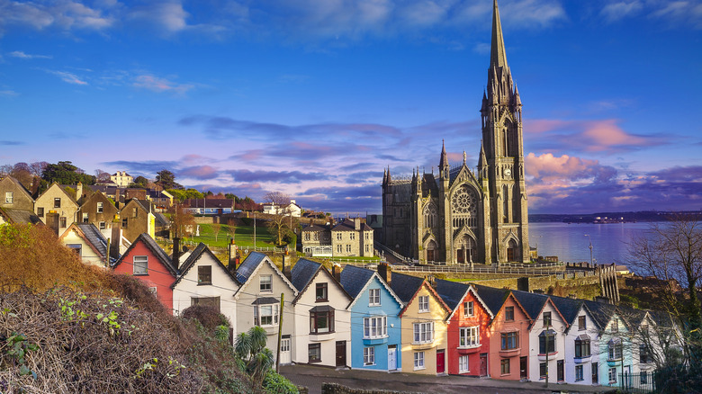 A row of brightly colored houses along a steep street in front of a cathedral in Cobh.