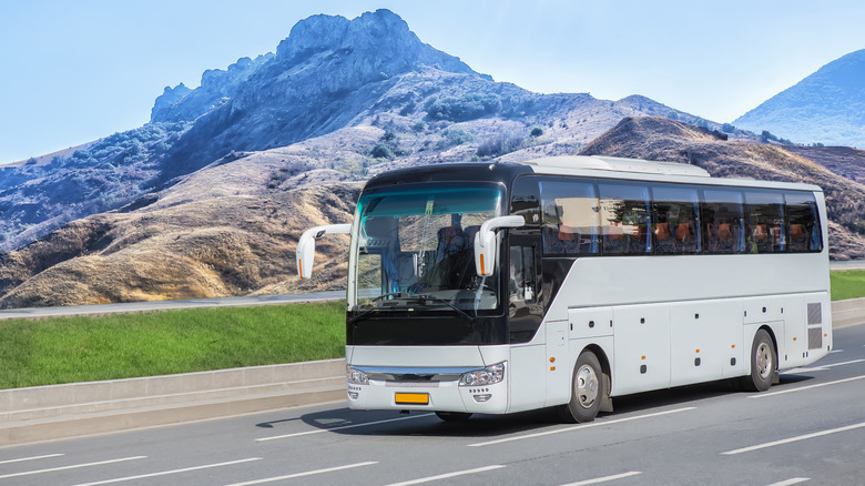 Tour bus on the highway with mountains in the background.