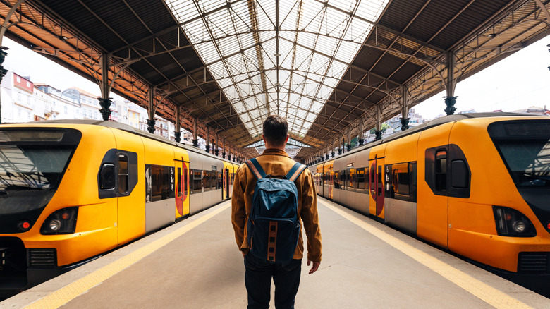 A man with a backpack standing between two trains on a platform