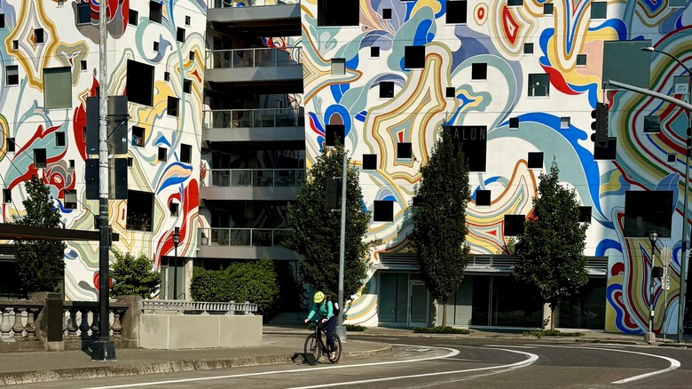 person riding bike on street with mural on building