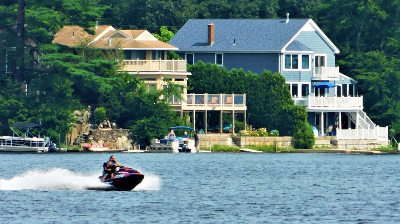 A jetskier zooms along the water in front of two upscale waterfront properties on Lake Chaubunagungamaug