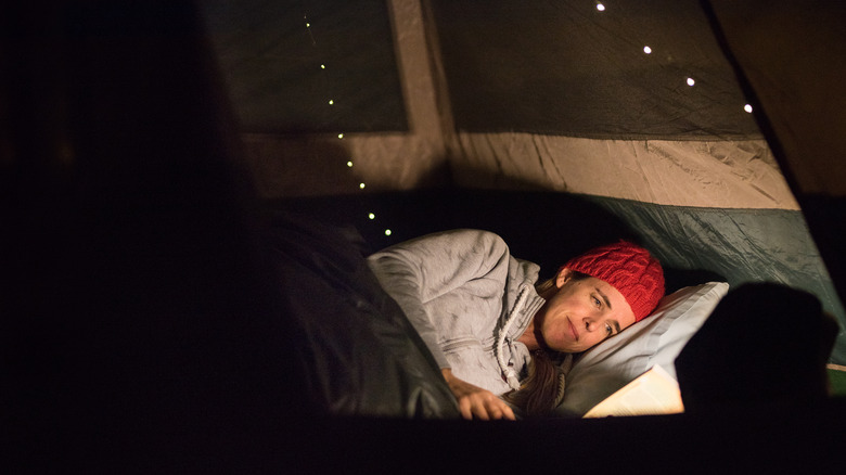 A woman reading in her tent, resting her head on a pillow