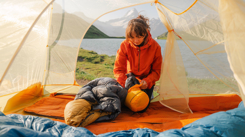 A woman in a tent unpacking her sleeping bag with a lake and mountain in the background