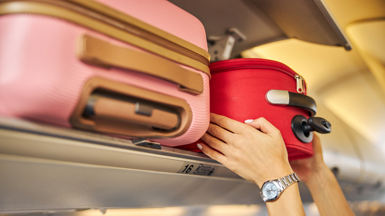 A person squeezes a piece of carry-on luggage into the overhead compartment of a plane
