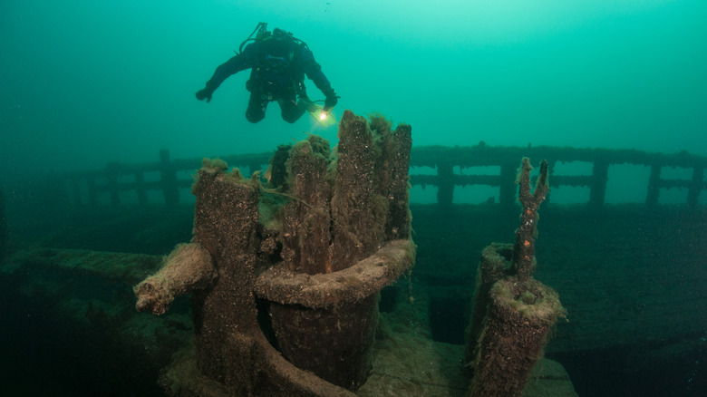 A scuba diver underwater shines a flashlight on a shipwreck in Lake Michigan