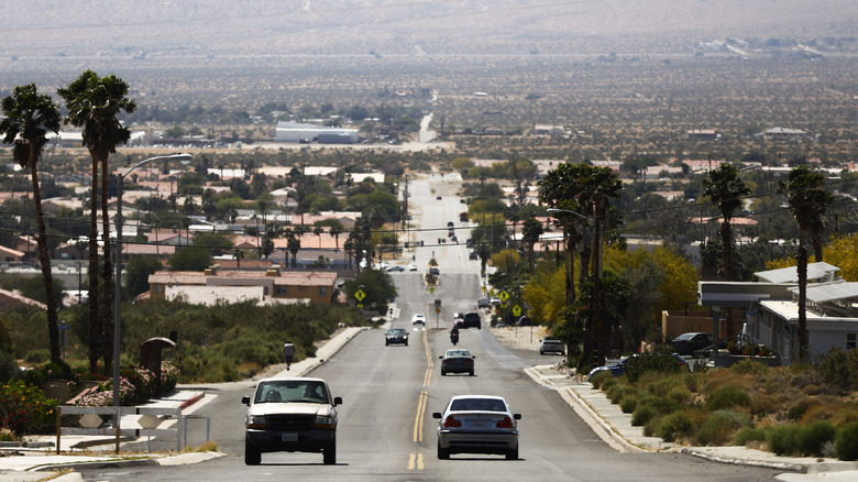 Cars driving on the road in the Coachella Valley near Desert Hot Springs, California, surrounded by palm trees and houses