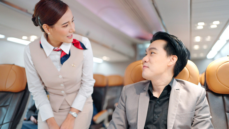 An asian man talking to a stewardess on a plane.