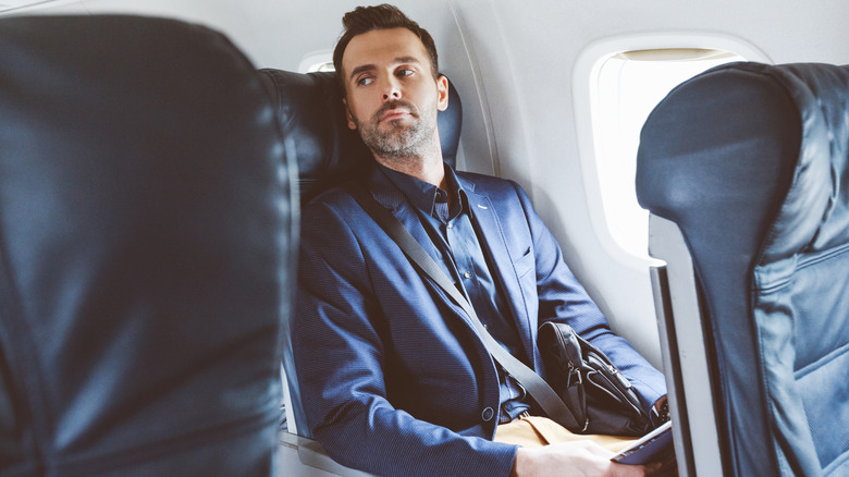 A stern man in a navy suit sitting in business class on a plane.