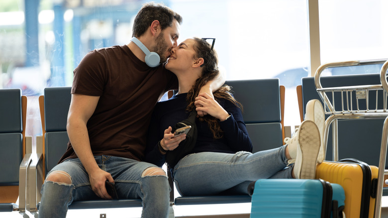 A newlywed couple kissing in an airport surrounded by their luggage.