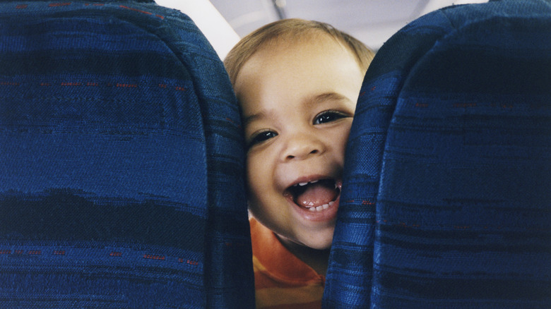 Smiling baby looking in between the seats on a plane.