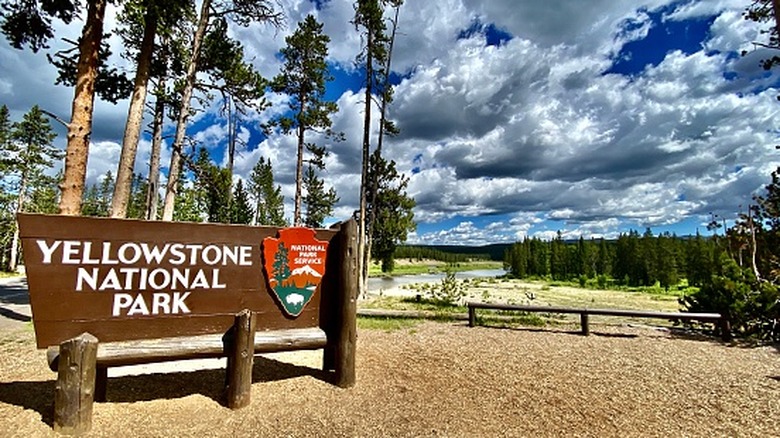 The sign at an entrance to Yellowstone National Park, surrounded by trees and a river
