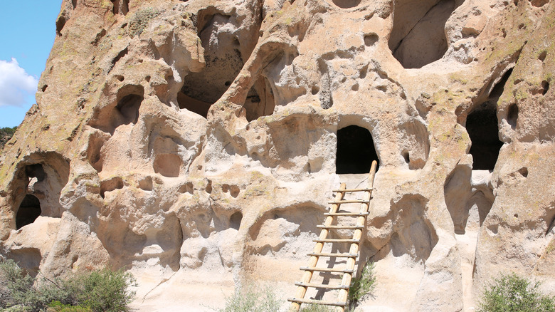 A rustic wooden ladder leading to a dark opening in the rocks in Bandalier National Monument in New Mexico