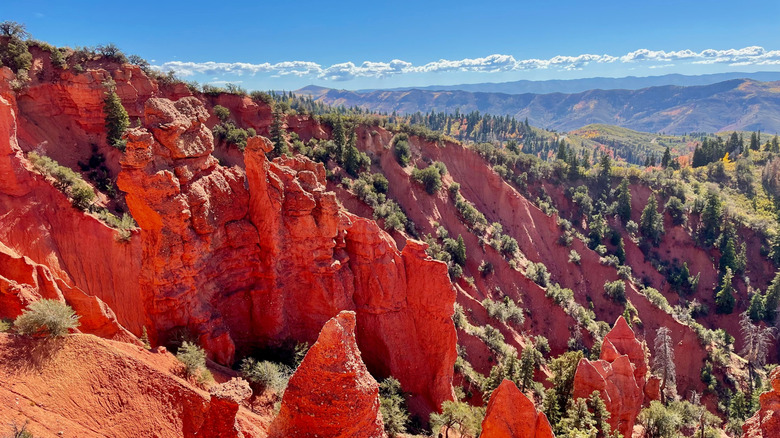 Shot ofred rocks, green trees, with mountains in the distance in Devil's Kitchen from the Nebo Loop Byway