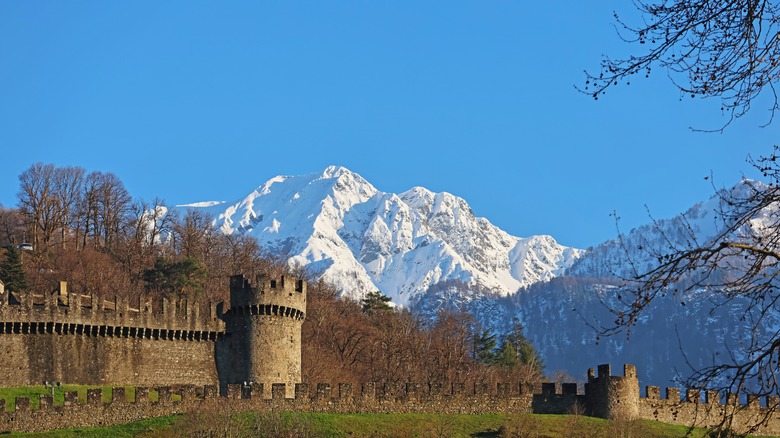Medieval castle walls with snow-capped Alpine peaks far away