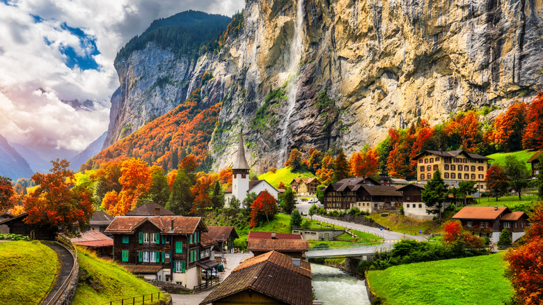 Swiss chalets against the backdrop of waterfalls cascading down a steep mountain slope dressed in fall colors